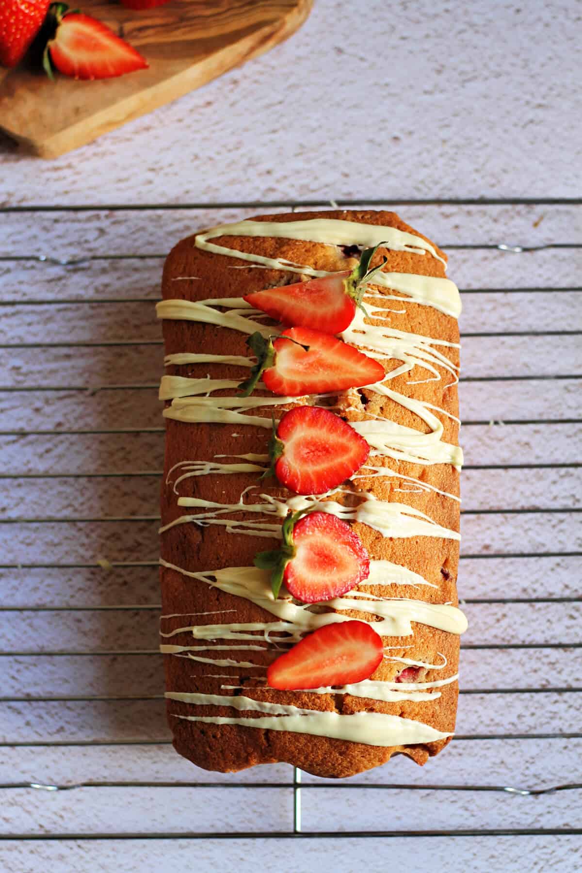Loaf cake with drizzles of white chocolate and sliced strawberries on top.