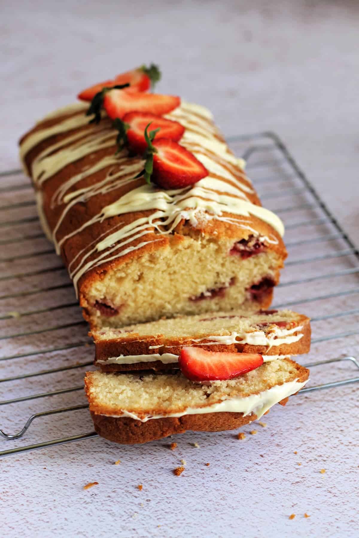 Loaf cake on a cooling rack with 2 cut slices, showing strawberries inside.