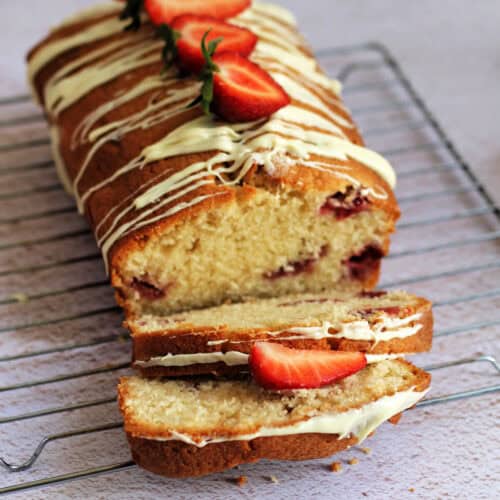 Loaf cake on a cooling rack with 2 cut slices, showing strawberries inside.