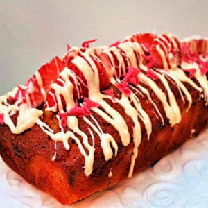 Loaf cake with strawberries and white chocolate drizzled over it.