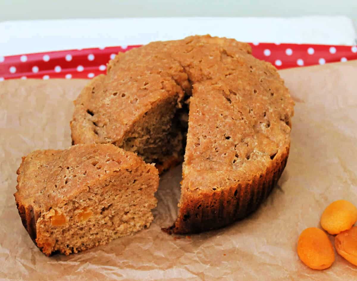 A round wholemeal apricot cake on baking paper, with one slice cut out.