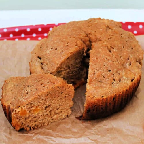 A round wholemeal apricot cake on baking paper, with one slice cut out.
