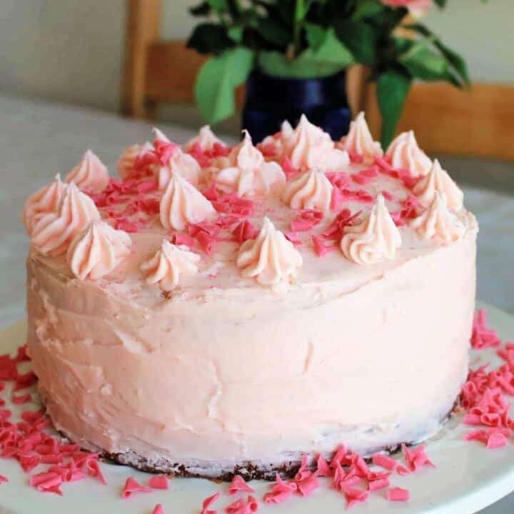 Strawberry cake with piped icing decoration on a table, roses behind in vase.