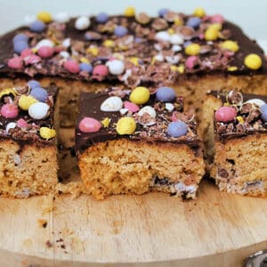 Mini egg blondies with chocolate layer and mini eggs on top, on wooden board.