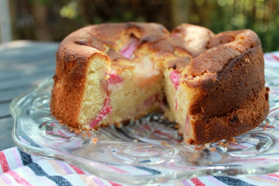 Rhubarb vanilla cake with a large slice removed, showing the pink rhubarb chunks inside.