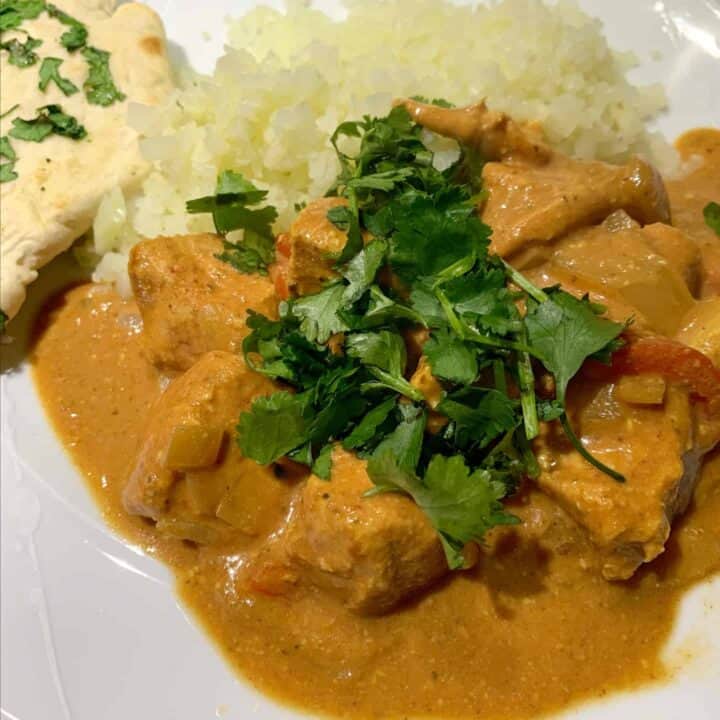Close-up of chicken curry on a white plate topped with coriander.