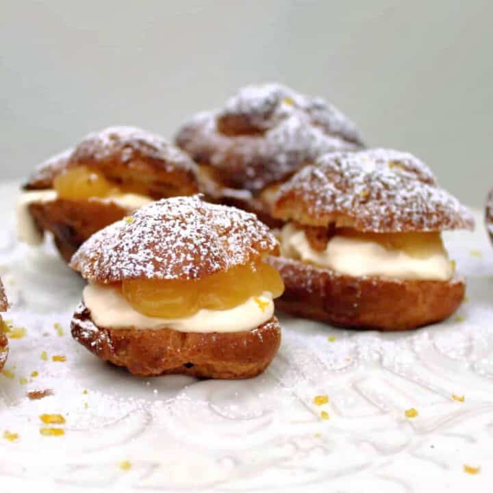 Choux buns with cream and lemon curd filling on white plate.