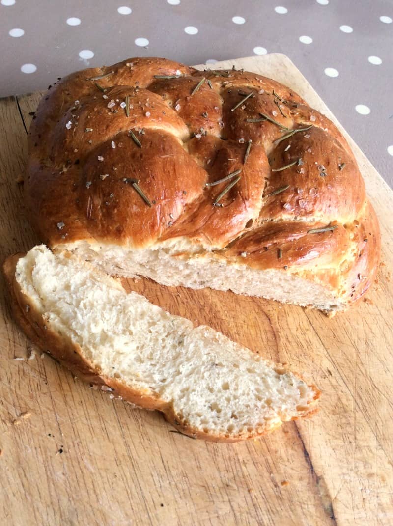 Loaf of bread with slice cut open on wooden board.