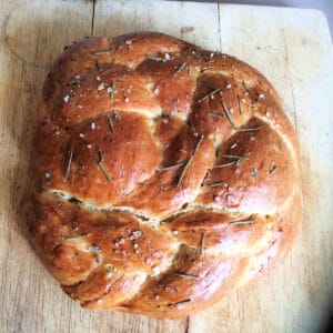 Loaf of braided rosemary bread on a board.
