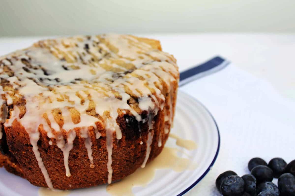 Cake with drizzles of icing, on a white plate with blueberries.