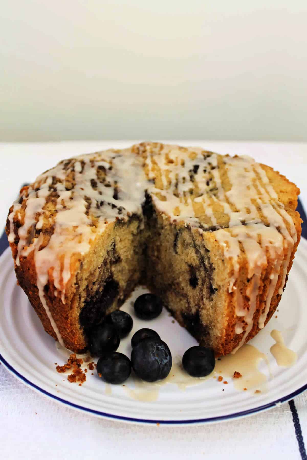 Blueberry marble cake with drizzles of icing, on a white plate with blueberries, with a slice removed.