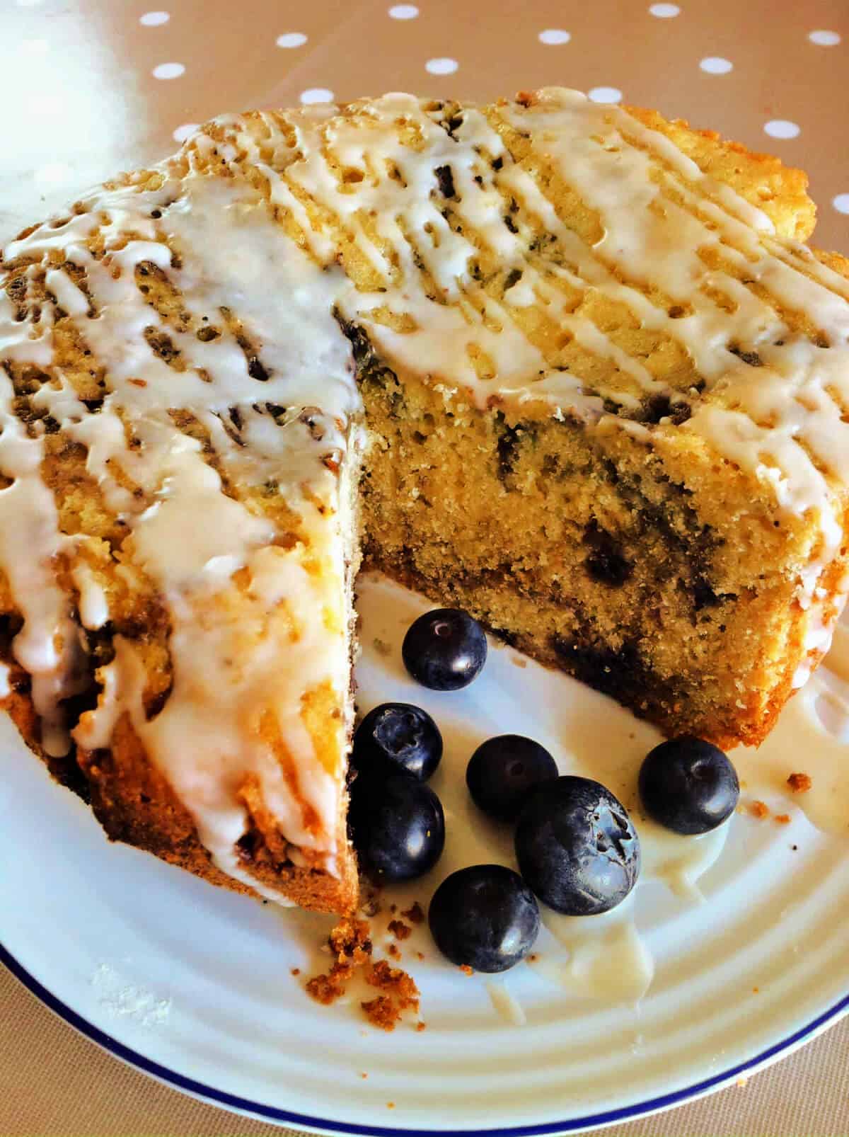 Blueberry marble cake with drizzles of icing, on a white plate with blueberries.