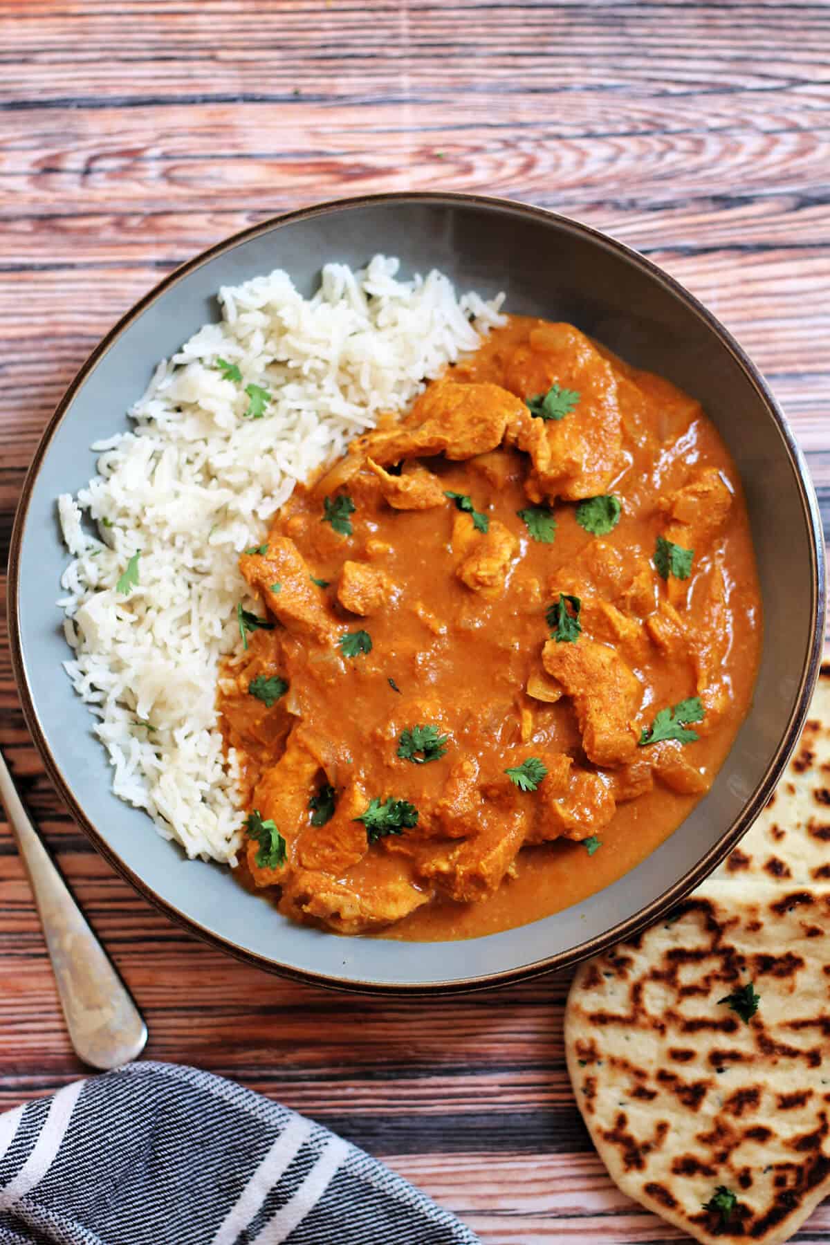 Chicken curry and rice in grey bowl, naan bread beside it.