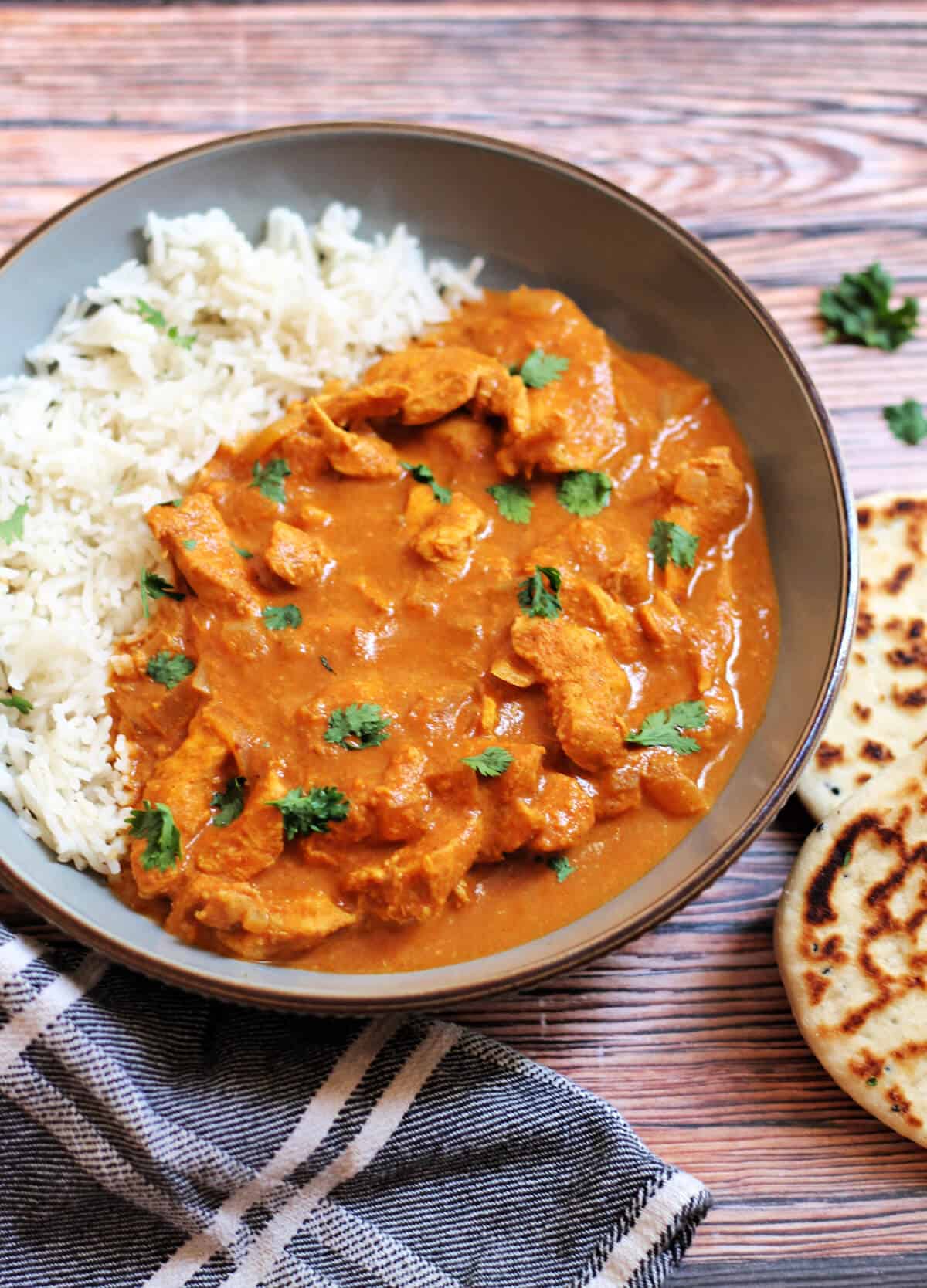 Chicken curry in a grey bowl with coriander garnish and naan beside.