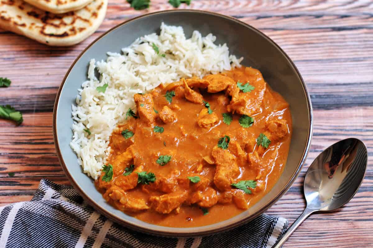 Bowl of curry and rice with cloth and spoon to the side, naan in background.