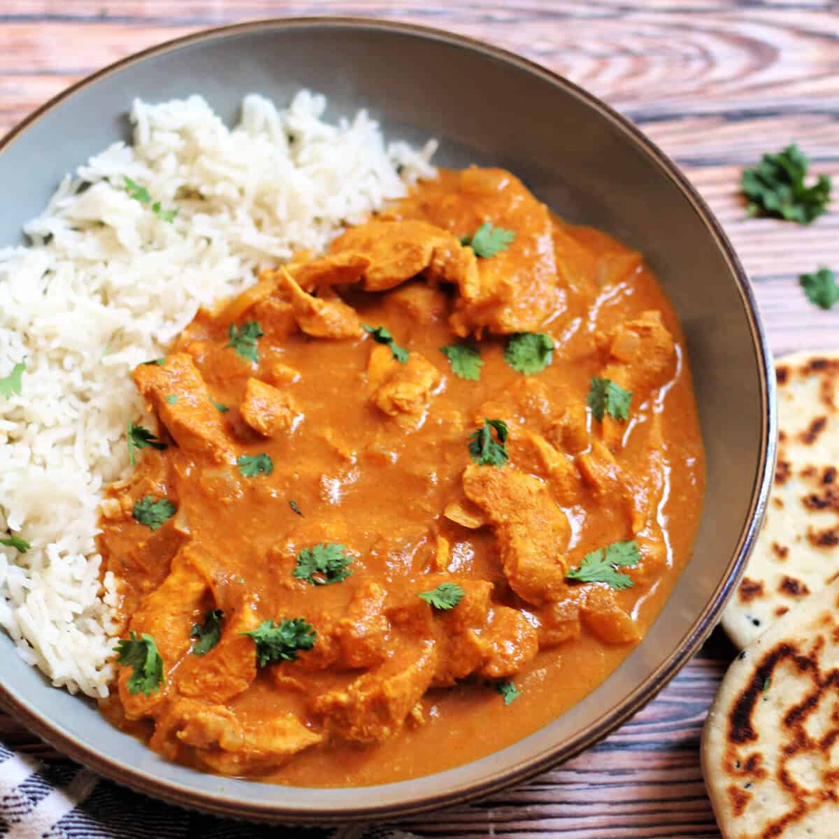 Chicken curry garnished with coriander in a grey bowl with rice.