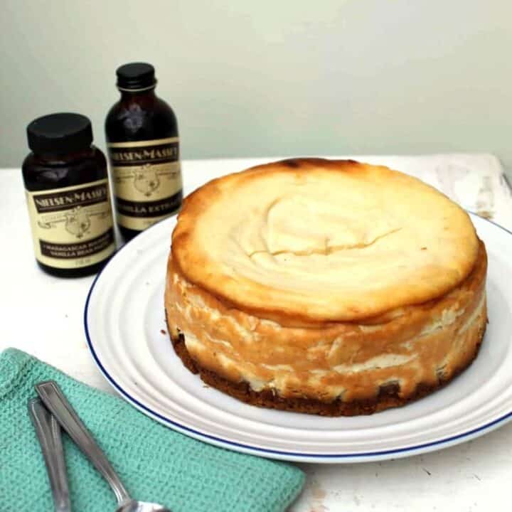 Vanilla cheesecake on a white plate with vanilla extract bottle to the side.