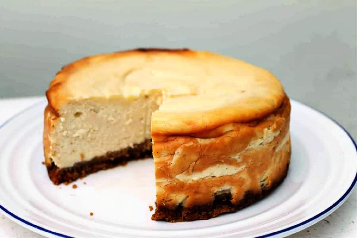 Close up of a cheesecake with a large slice cut out of it, on white plate.