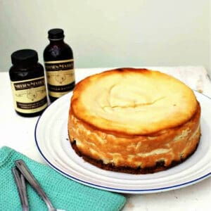 Vanilla cheesecake on a white plate with vanilla bottle to the side.