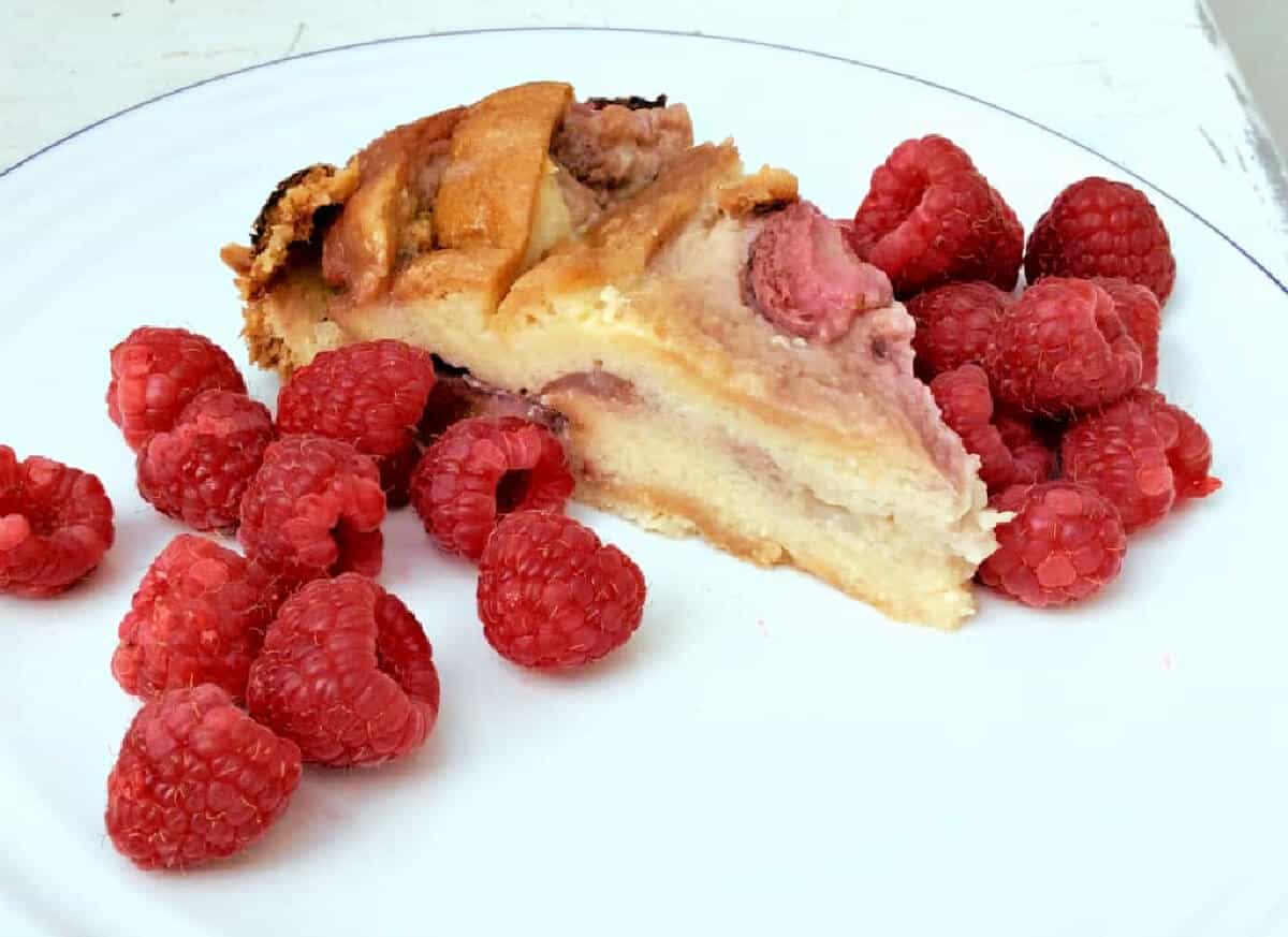 A slice of brioche strawberry pudding on a white plate with raspberries.