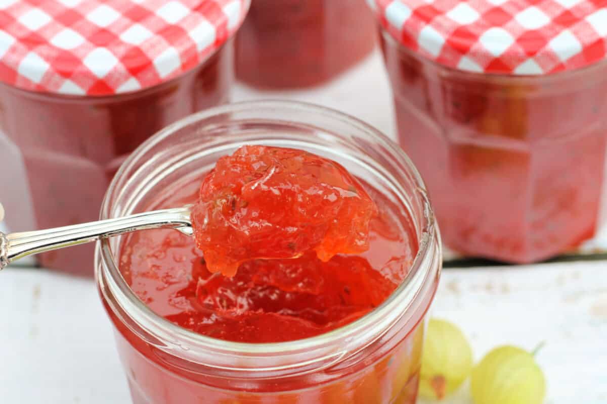 Spoonful of gooseberry jam over a jar of jam.