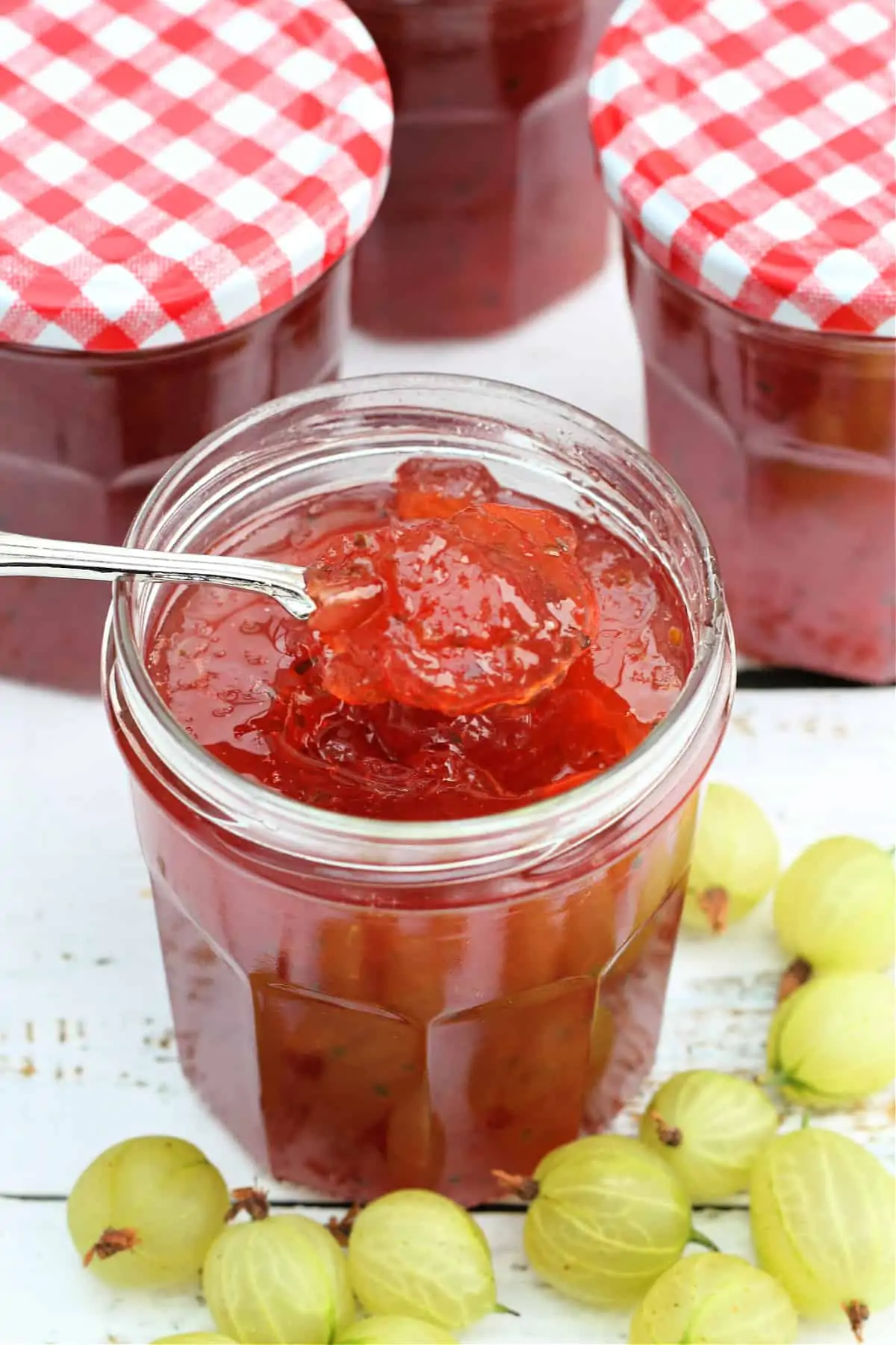 Spoon in jar of jam with gooseberries around it.