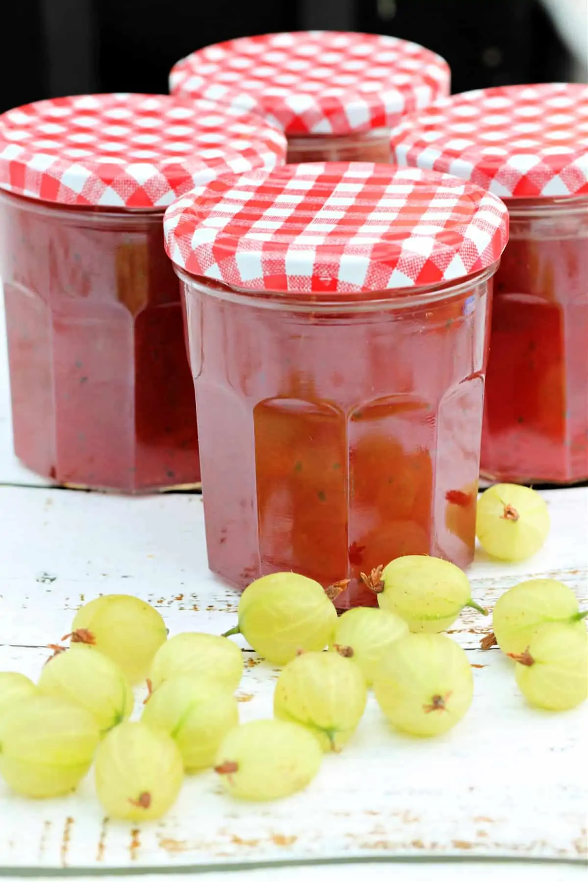 Jars of jam with gooseberries in front.