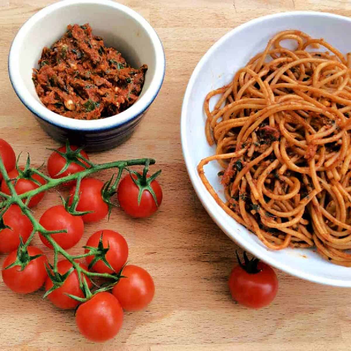 Bowl of spaghetti, vine tomatoes and pot of red pesto.