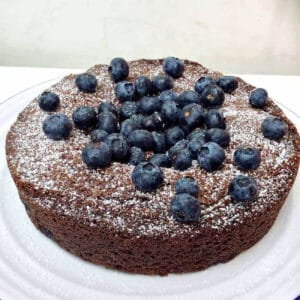 Chocolate cake with blueberries and dusted with icing sugar on a white plate.