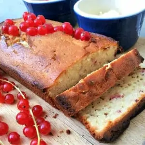 Redcurrant yoghurt loaf cake with fresh redcurrants on top, two slices cut out.
