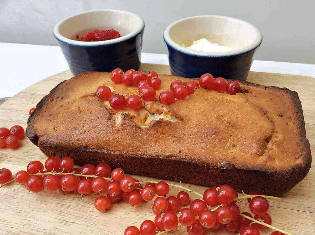 Loaf cake topped with redcurrants on chopping board.