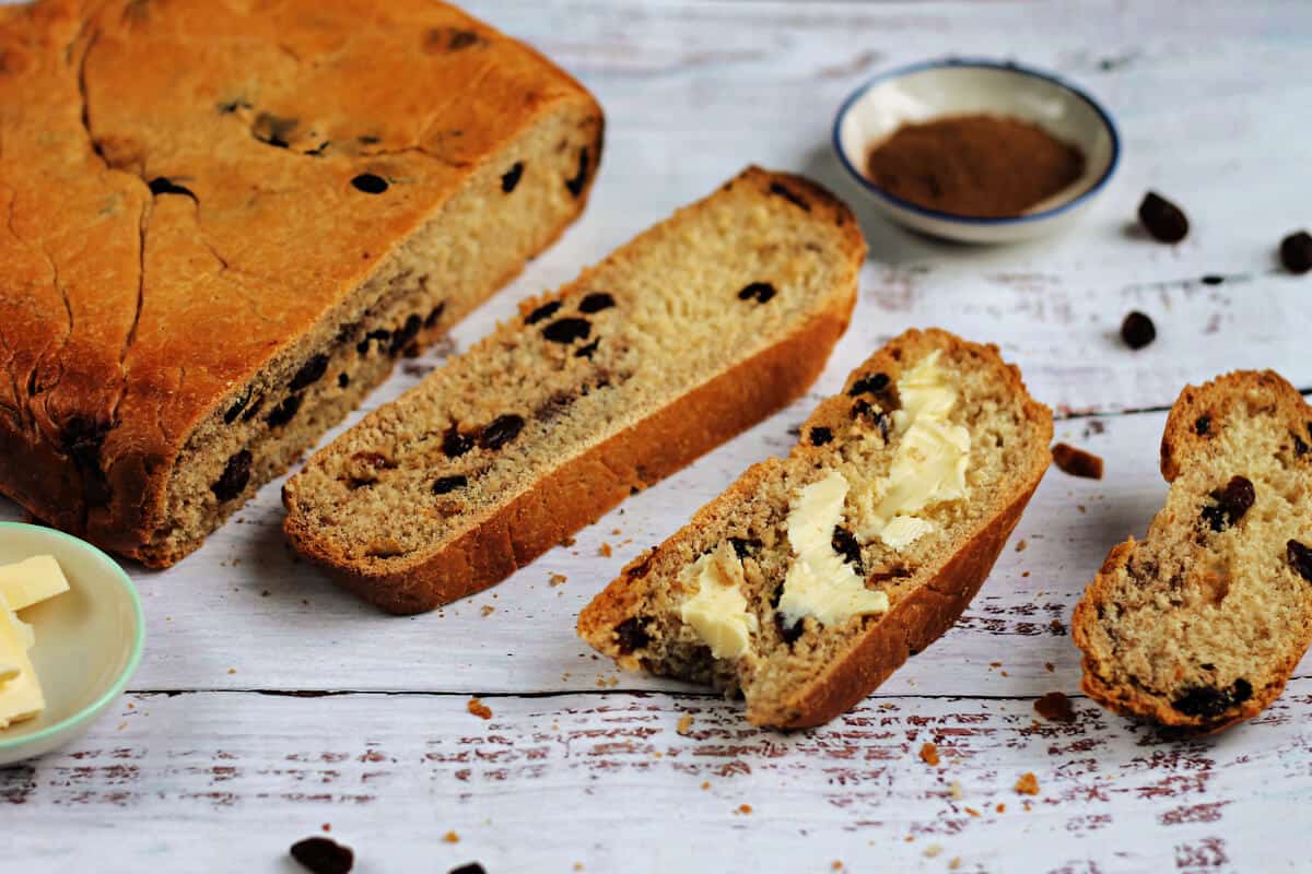 Buttered slice of cinnamon raisin bread next to sliced loaf.