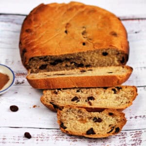 Sliced loaf of cinnamon raisin bread with raisins beside it.