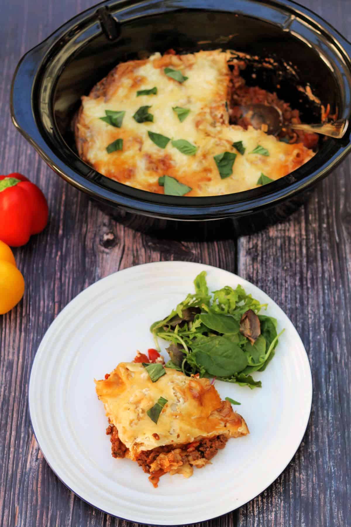 Lasagne in a serving dish with a plate to the front with a portion with salad.