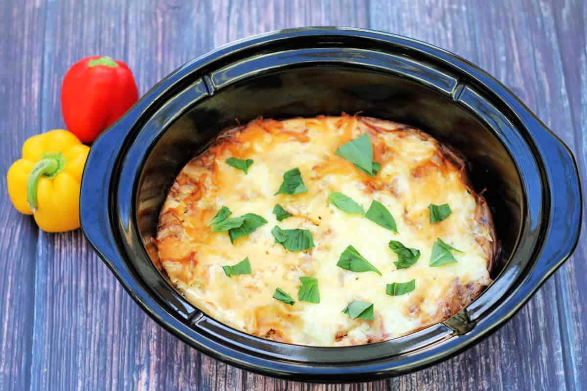 Cooked lasagne in slow cooker pot, garnished with basil.