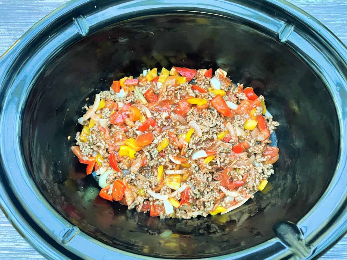 Slow cooker pot with a layer of meat sauce.