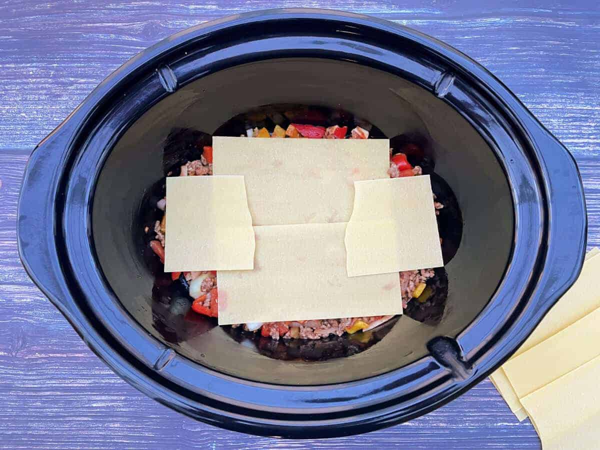 Slow cooker pot with meat sauce with lasagne sheets layered on top.