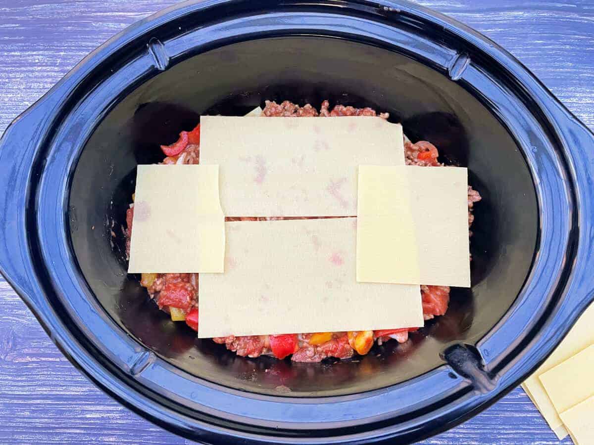 Layers of meat sauce and pasta sheets in a slow cooker pot.