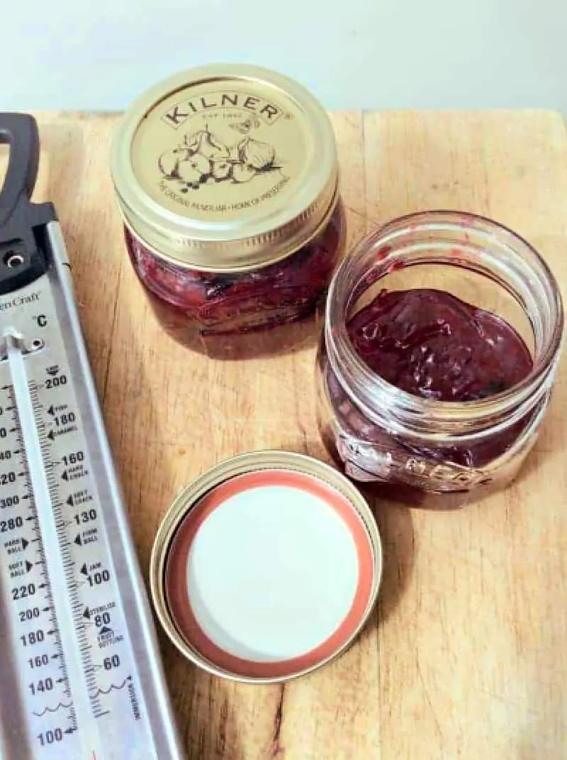 Jars of jam and sugar thermometer on a wooden board.