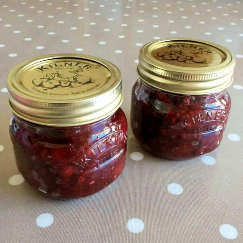 Two small jars of jam on a brown background with white dots.
