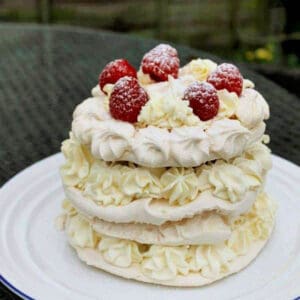 Layered meringue cake with piped cream topped with raspberries on a white plate.