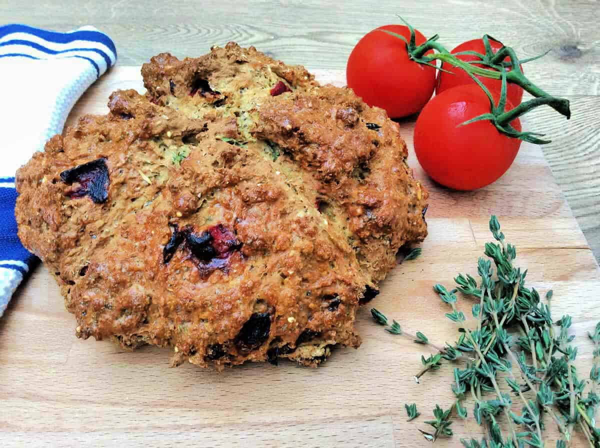 Soda bread on a wooden chopping board, tomatoes in background.