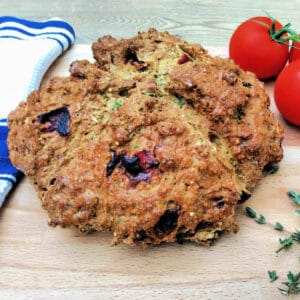 Soda bread on a wooden chopping board, tomatoes in background.