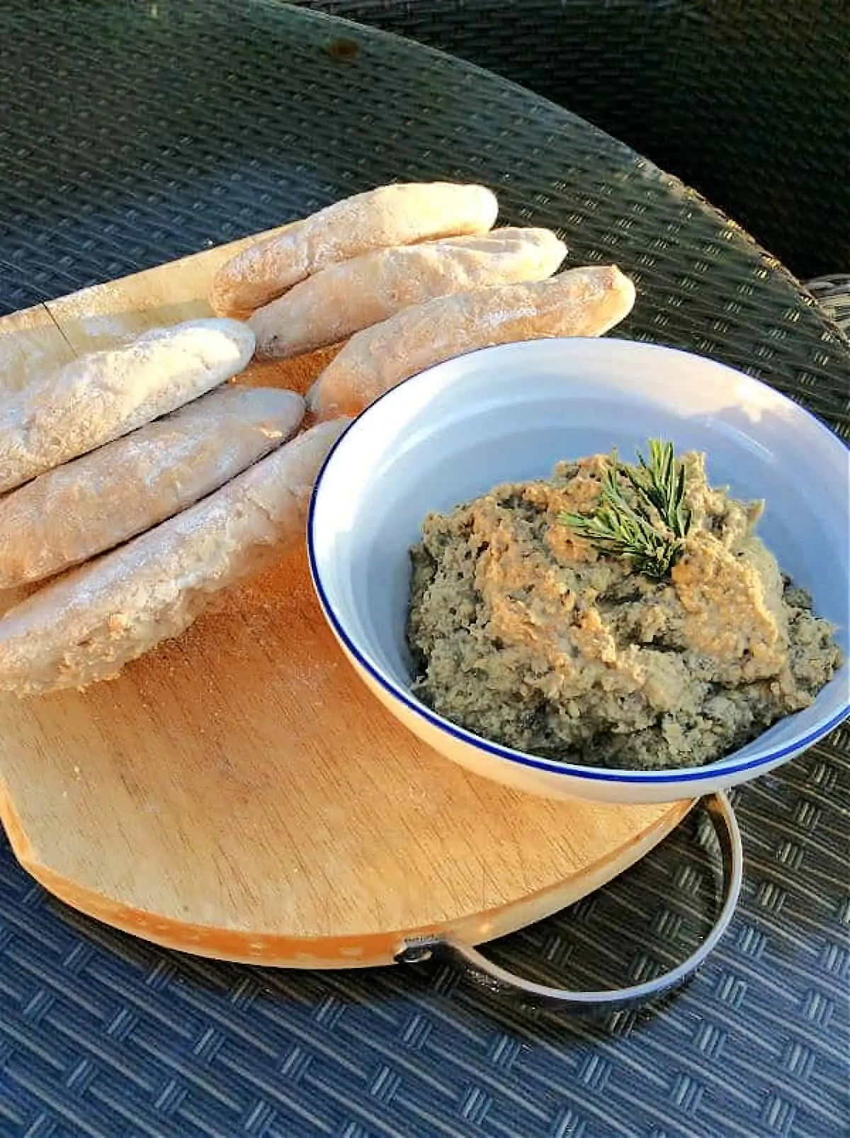 Bowl of hummus on a wooden board with pitta breads.