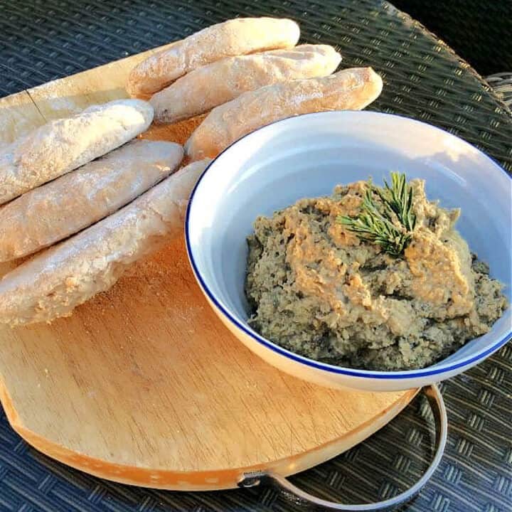 White bowl of hummus with pitta breads.