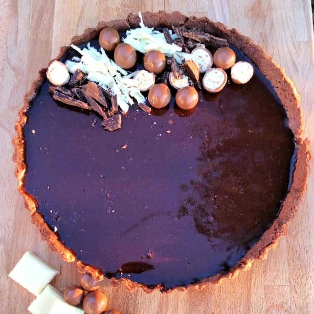 Chocolate tart with mirror glaze and chocolate decorations on wooden board.