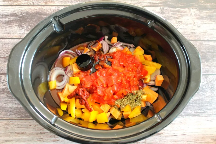 Vegetables with tinned tomatoes and stock pot in slow cooker pot.