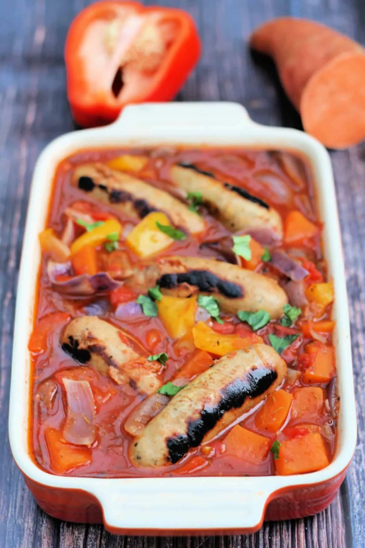 Sausage and vegetable casserole in a serving dish on a wooden background.