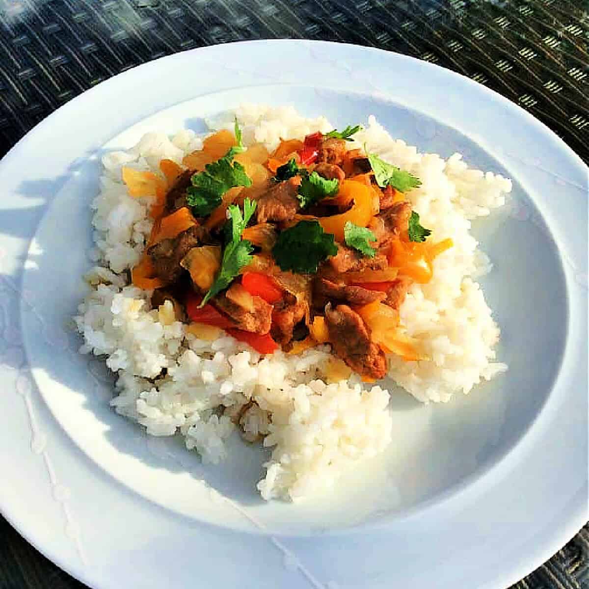 Pork with pepper on rice with chopped coriander, on a white plate.