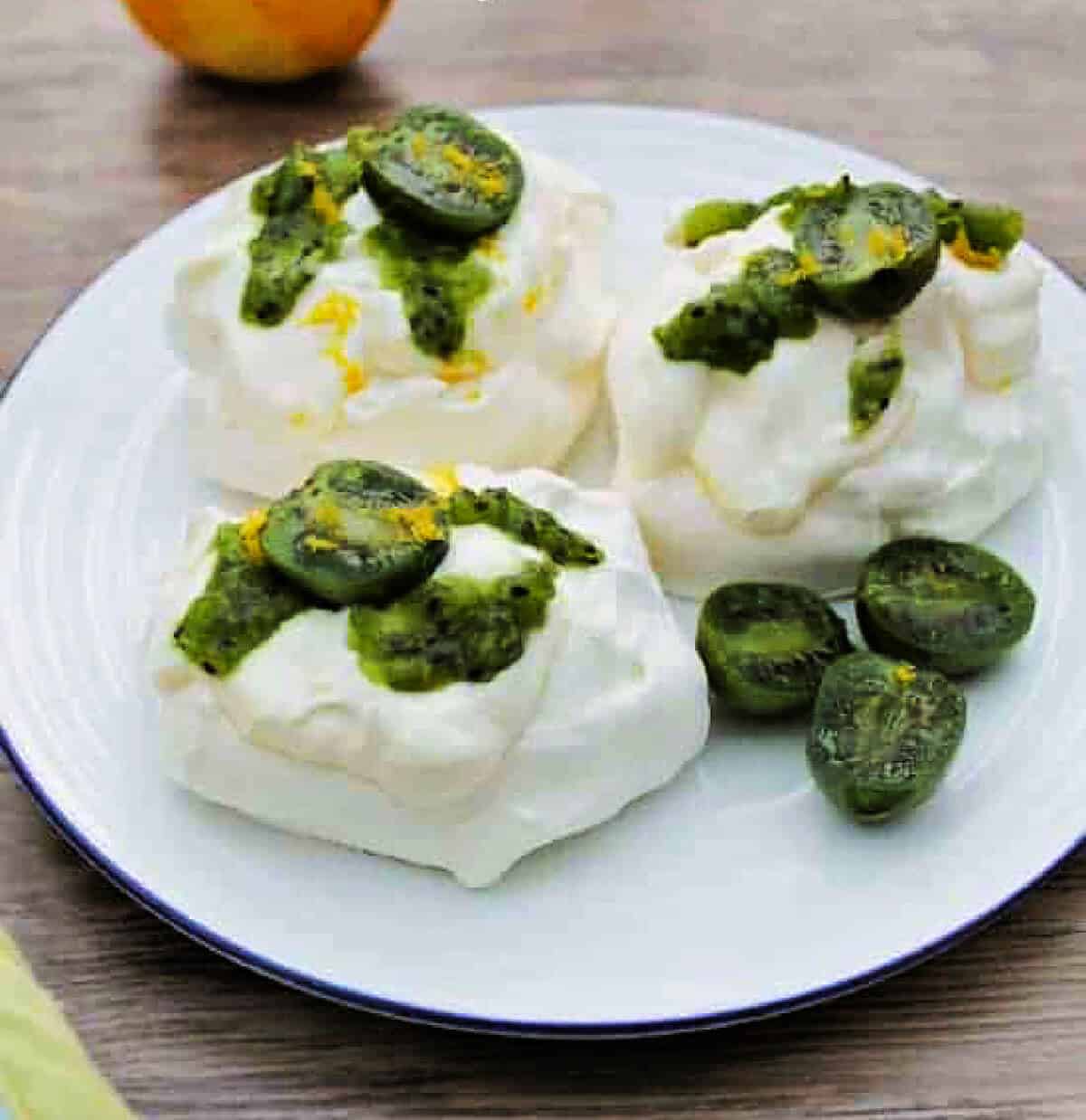 Meringue shells topped with cream and green berries on white plate.